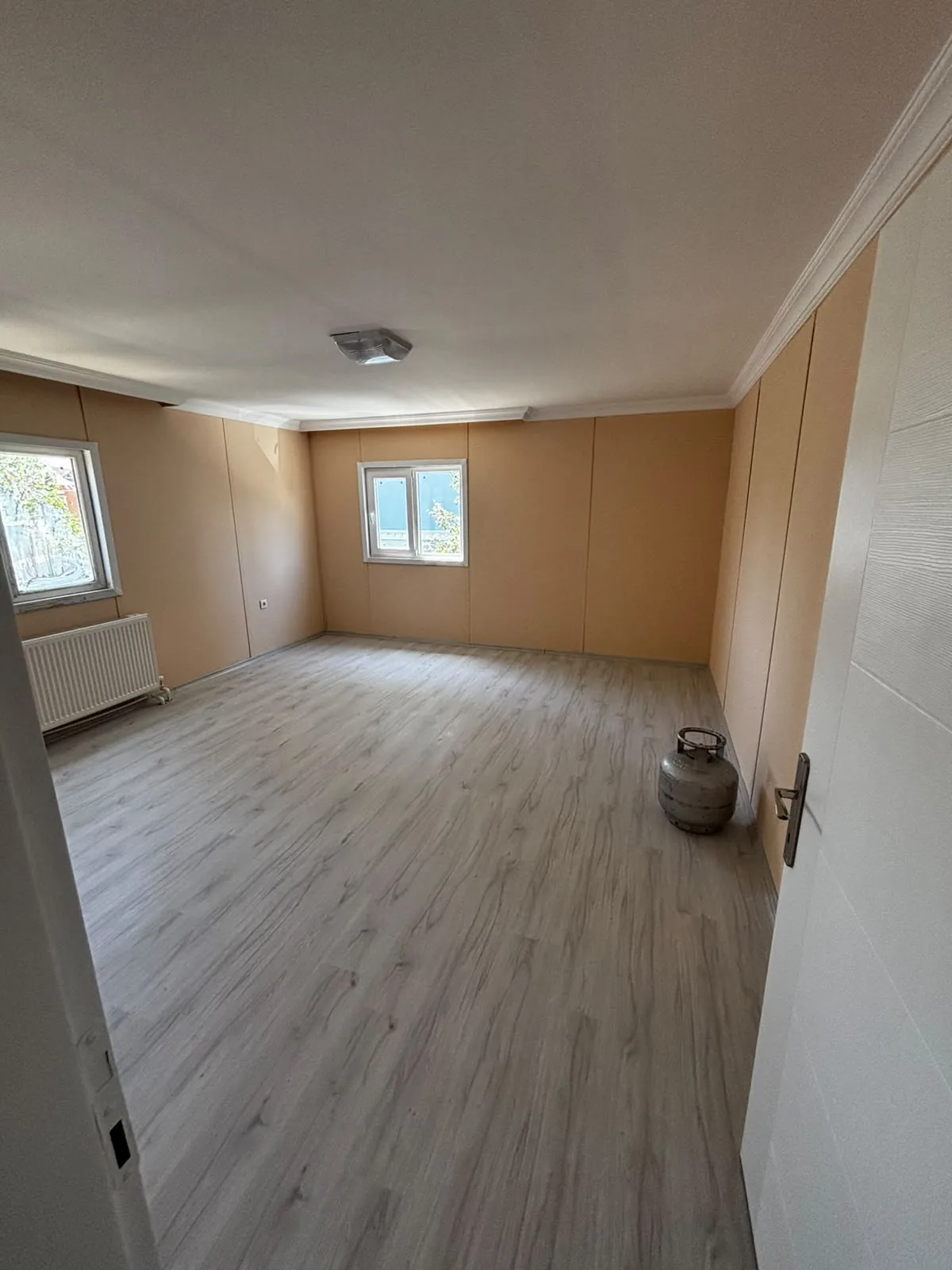 Laminat parke, radyatör, PVC pencereler ve kartonpiyer bulunan boş prefabrik ev odası