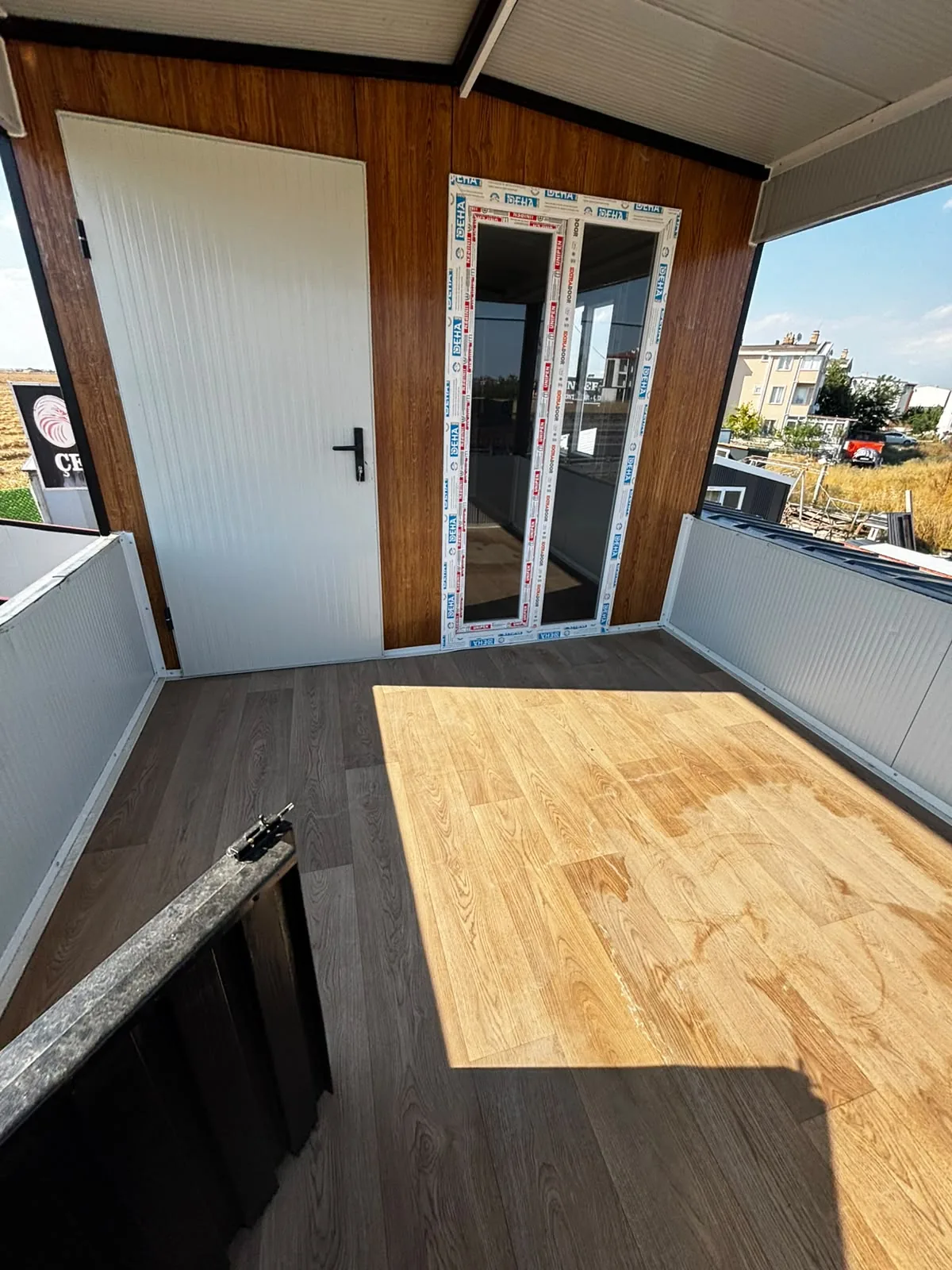 Ahşap desenli teraslı konteynerin üst katında, çatı altında bulunan balkon ve giriş kapısı
